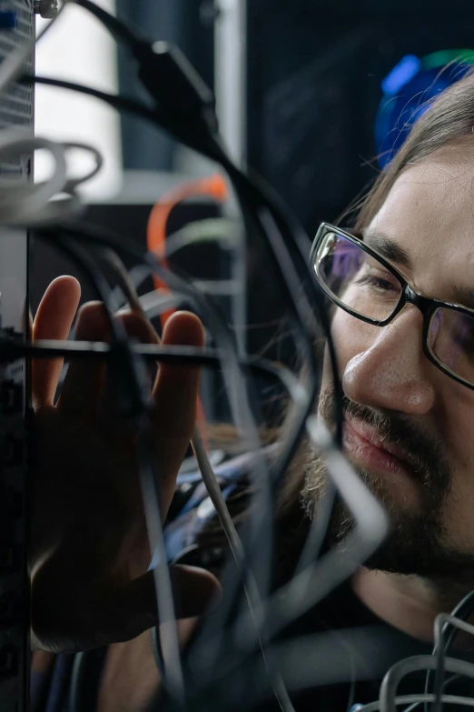 a man standing in front of a bunch of wires, with glasses and goatee, future coder looking on, a close-up, digging