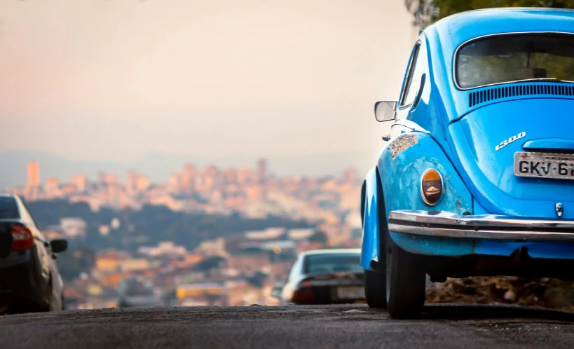 a blue vw beetle parked on the side of a road, by Matt Stewart, pexels contest winner, photorealism, looking over city, sao paulo, an ancient, overlooking