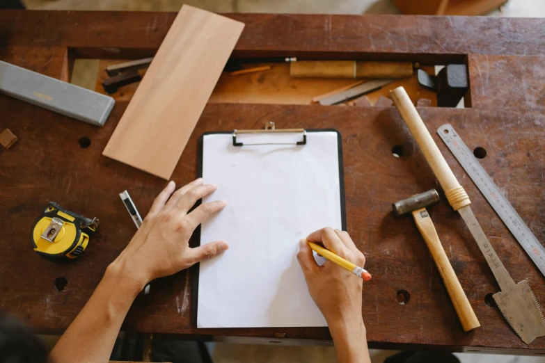 a person holding a pencil and writing on a piece of paper, pexels contest winner, arbeitsrat für kunst, wooden furniture, clipboard, mechanics, jovana rikalo