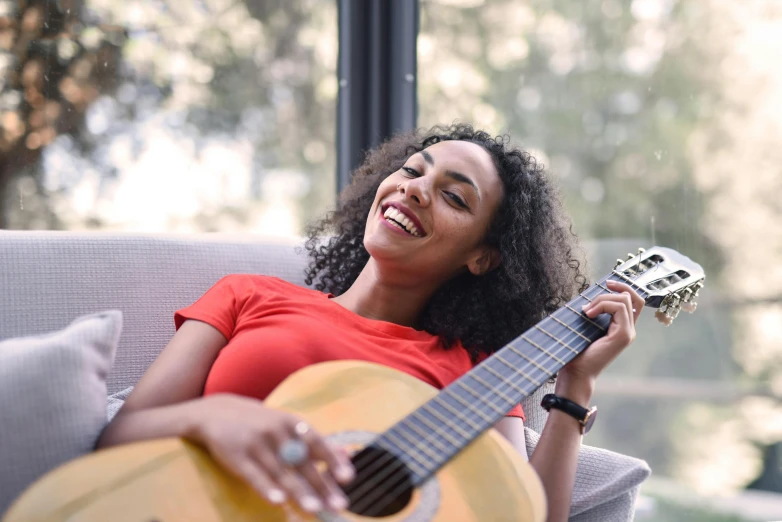 a woman sitting on a couch holding a guitar, pexels contest winner, happening, mixed-race woman, avatar image, small wide smile, profile pic