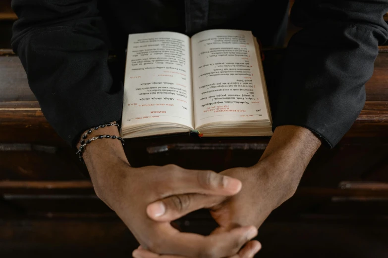 a close up of a person holding an open book, priest, black man, definition, thumbnail