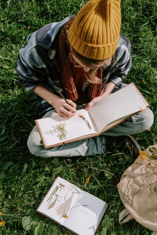 a woman sitting in the grass writing on a book, a drawing, pexels contest winner, visual art, botanicals, top down drawing, an young urban explorer woman, mate painting