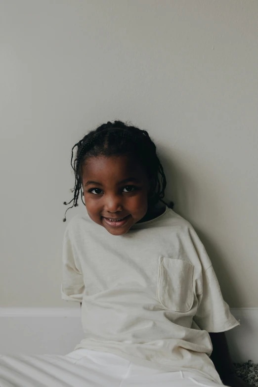 a little girl sitting on top of a bed, pexels contest winner, wearing a white sweater, dark skinned, boy with neutral face, leaning against the wall