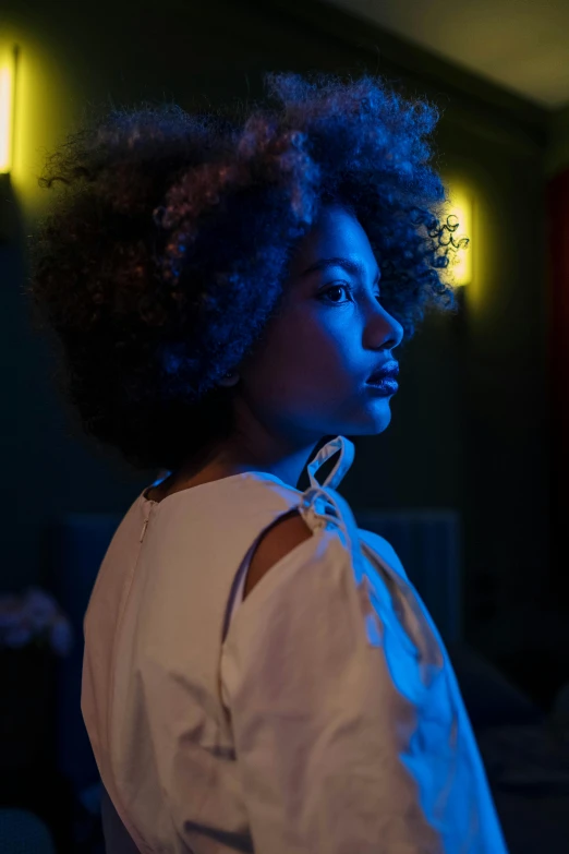 a woman standing in a dimly lit room, inspired by Nan Goldin, pexels contest winner, afrofuturism, dramatic white and blue lighting, with afro, light skinned african young girl, portrait color glamour