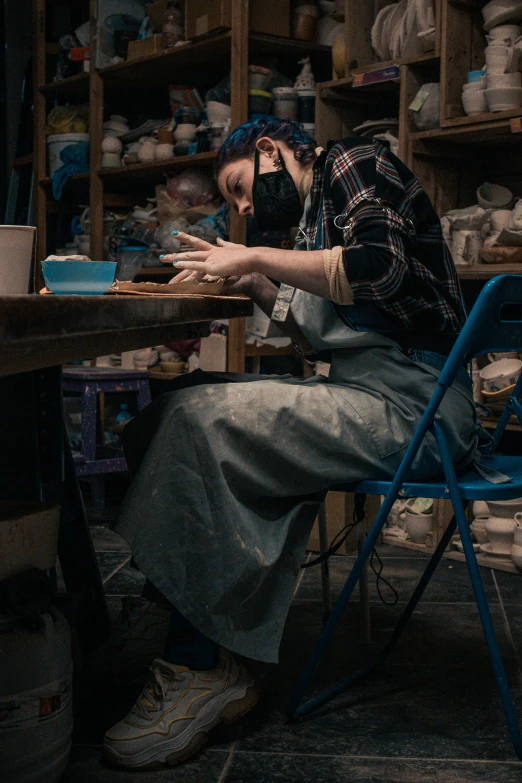 a man sitting at a table working on a piece of pottery, a portrait, by Charlotte Harding, pexels contest winner, wearing facemask, woman in a dark factory, dipped in polished blue ceramic, 2 0 2 2 photo