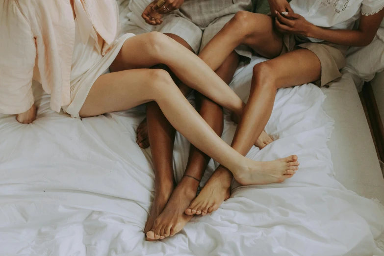a group of women sitting on top of a bed, trending on pexels, thigh skin, neutral colours, holding each other, bare leg