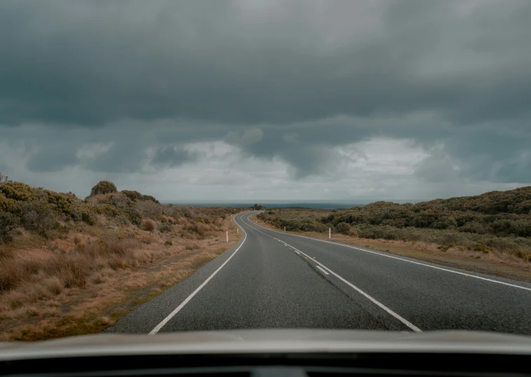 a car driving down a road on a cloudy day, by Jessie Algie, unsplash, lachlan bailey, looking onto the horizon, high quality photo, thumbnail