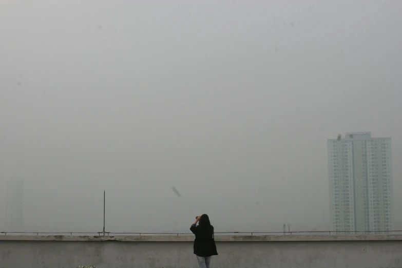 a person standing on top of a roof flying a kite, inspired by Zhang Kechun, postminimalism, smog, hangzhou, camera looking up at her, background image