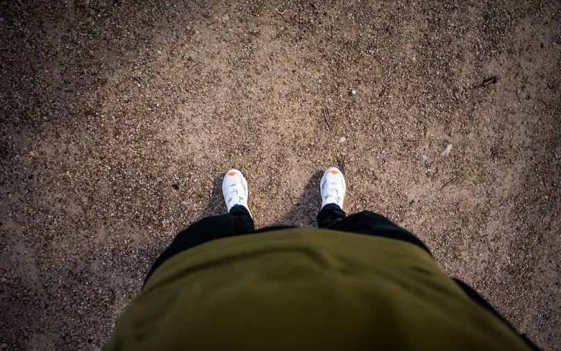 a person standing in the middle of a dirt road, wearing white sneakers, looking from slightly below, outside in parking lot, intimidating floating sand