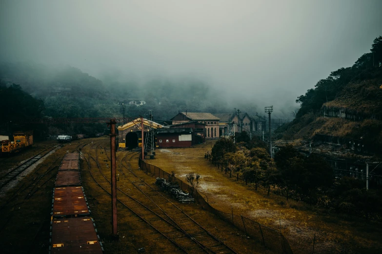 a train traveling down train tracks next to a lush green hillside, a matte painting, by Elsa Bleda, pexels contest winner, magical realism, misty ghost town, gloomy earthy colors, train station, mining outpost