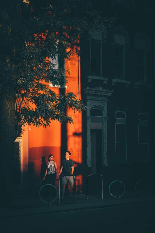 two people sitting on a bench in front of a building, a photo, by Andrew Domachowski, unsplash contest winner, orange light, standing outside a house, washington dc, red and blue back light