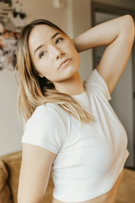 a woman standing in a living room next to a couch, inspired by Károly Lotz, trending on pexels, dressed in a white t shirt, headshot photoshoot, chloe bennet, natural beauty expressive pose
