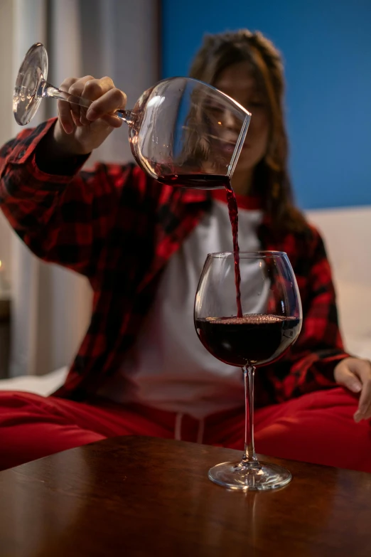 a woman sitting at a table pouring a glass of wine, sleepwear, red and blue color scheme, zoomed in, cascadian