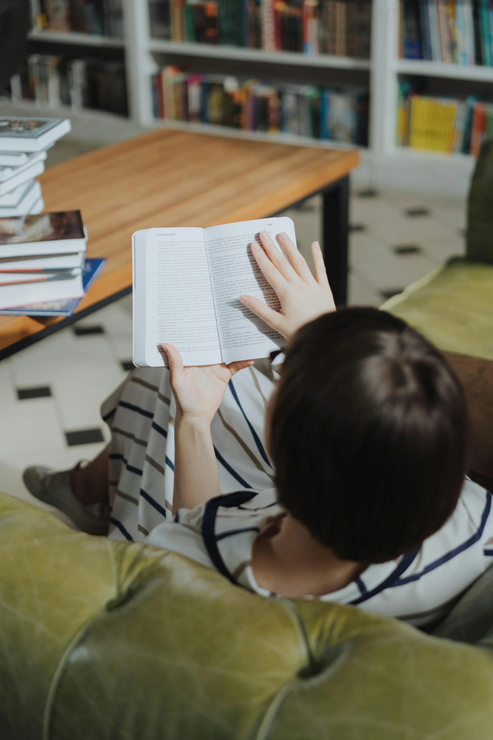 a woman sitting on a couch reading a book, happening, hand on table, very consistent, schools, curated collections