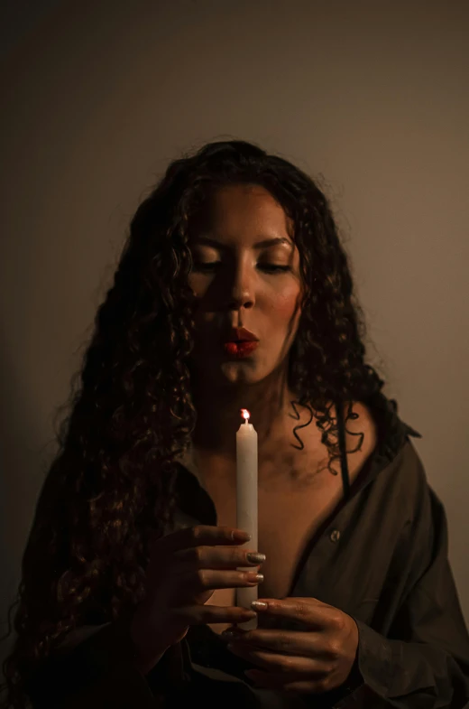 a woman holding a candle in front of her face, an album cover, lgbtq, deep lighting, ariel perez, looking towards camera