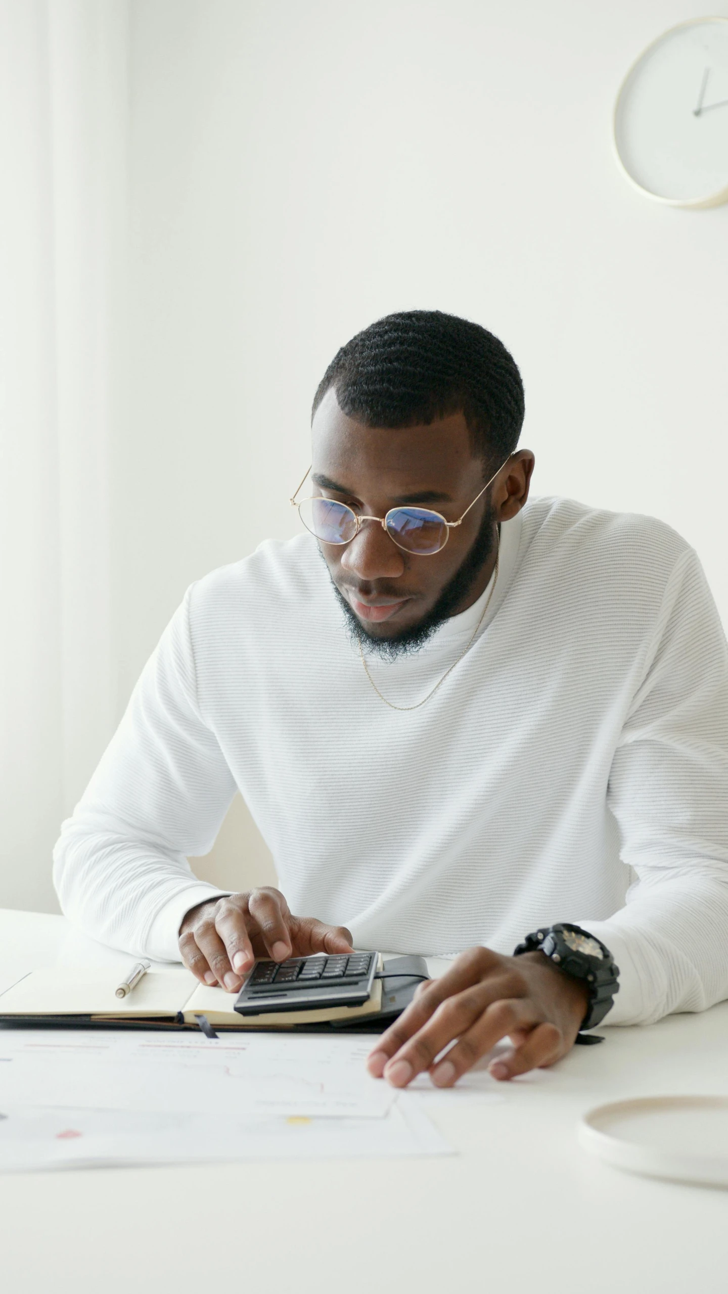 a man sitting at a table using a calculator, mkbhd, wearing round glasses, thumbnail, multiple stories