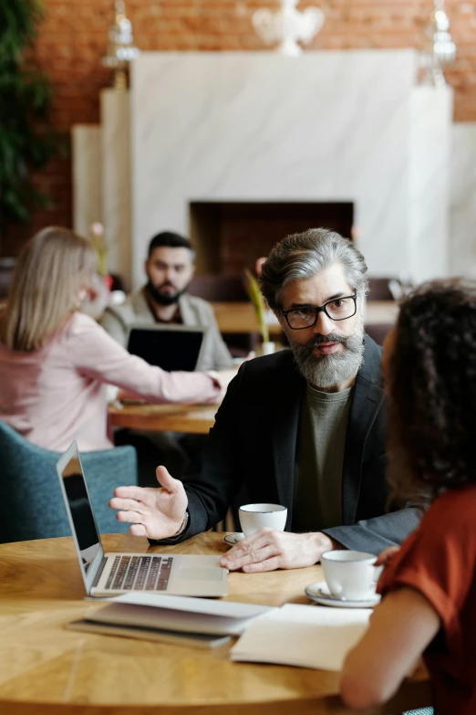 a group of people sitting around a table with laptops, trending on pexels, renaissance, gray beard, man with glasses, sitting on a mocha-colored table, ignant