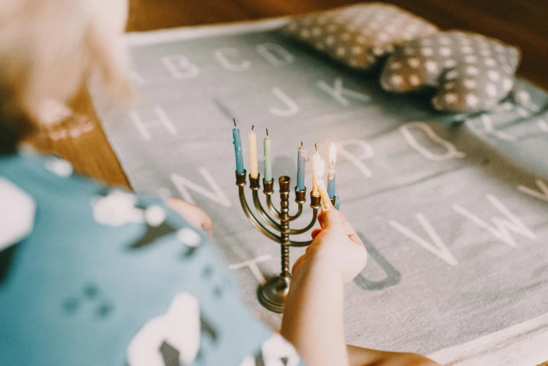 a little girl lighting a menorah on a table, by Julia Pishtar, trending on unsplash, art & language, light boho carpet, blue and grey theme, board games, wearing festive clothing