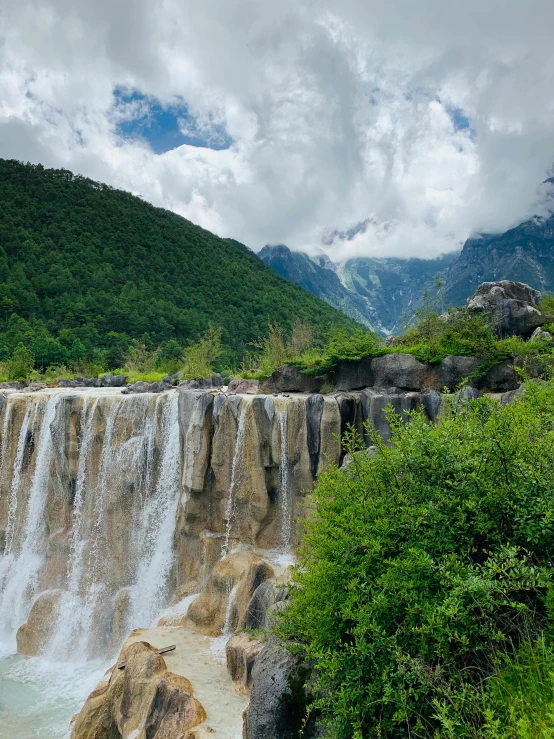 a waterfall in the middle of a lush green forest, inspired by Li Keran, hurufiyya, dramatic mountains behind, promo image, multiple stories, exterior shot