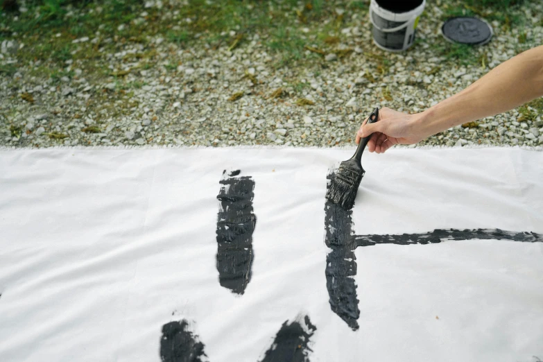 a person using a brush to paint letters on a sheet of paper, a silk screen, inspired by Colin McCahon, unsplash, action painting, vantablack cloth technology, nice weather, mina petrovic, wwf