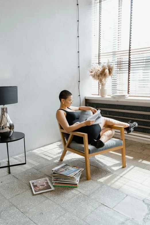 a woman sitting in a chair reading a book, inspired by Constantin Hansen, pexels contest winner, modernism, dwell, inspect in inventory image, magazines, small room