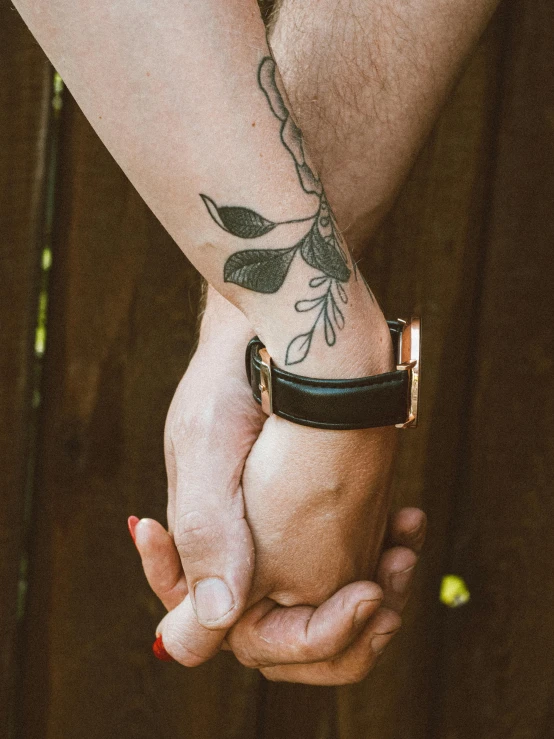 a couple holding hands in front of a wooden fence, a tattoo, by Julia Pishtar, trending on pexels, wrapped in leather straps, lgbtq, detailed product image, half image