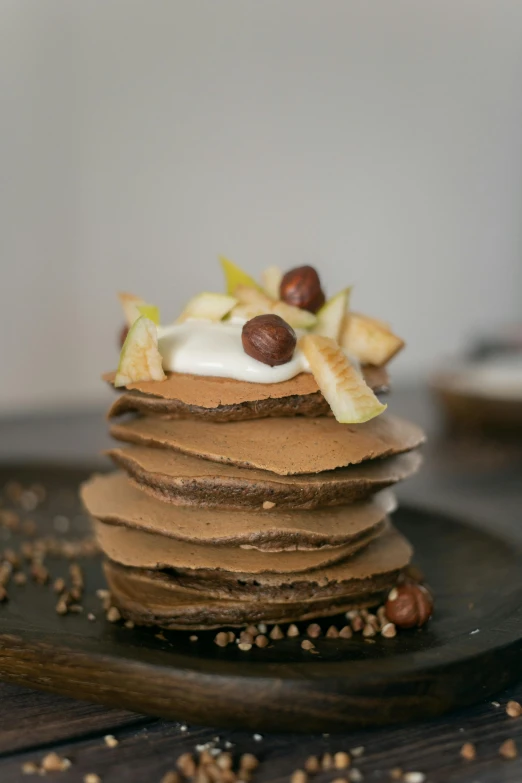 a stack of pancakes sitting on top of a black plate, inspired by Henriette Grindat, fully chocolate, nut, felt, fruit