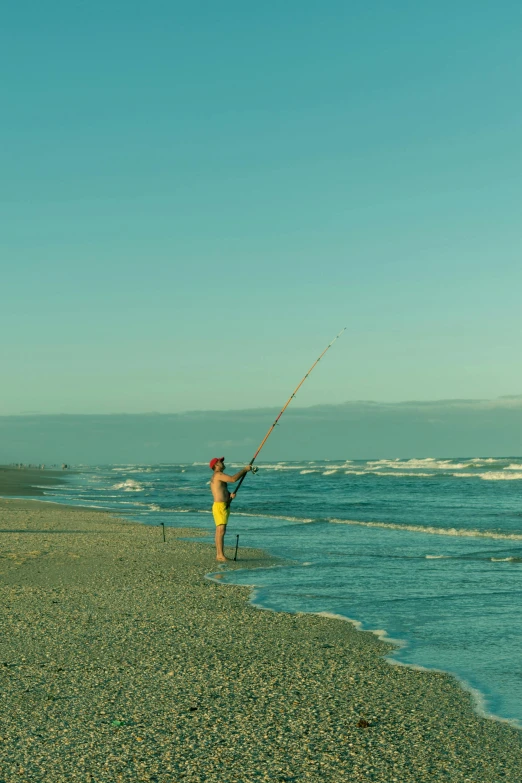 a man standing on top of a sandy beach next to the ocean, fishing pole, beach on the outer rim, ocean spray, south african coast