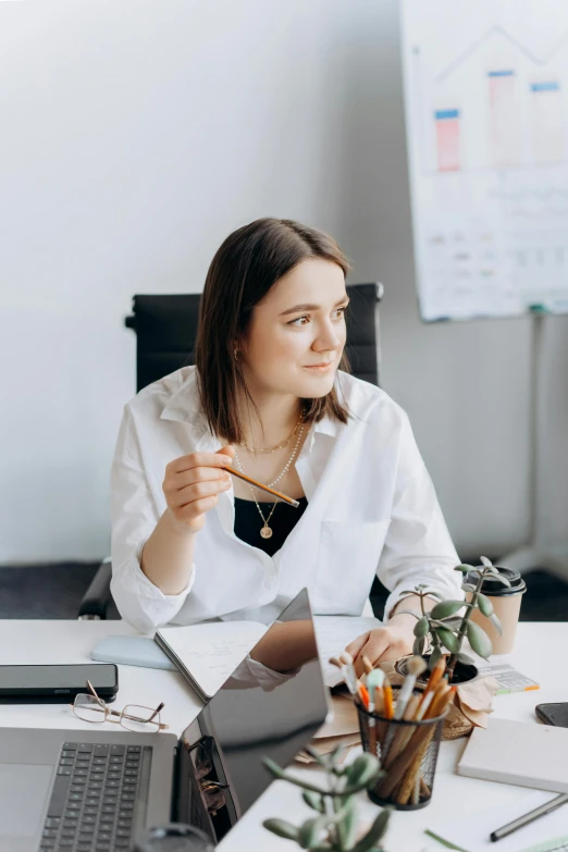 a woman sitting at a table in front of a laptop, wearing a white blouse, sat in an office, intricate quality, avatar image