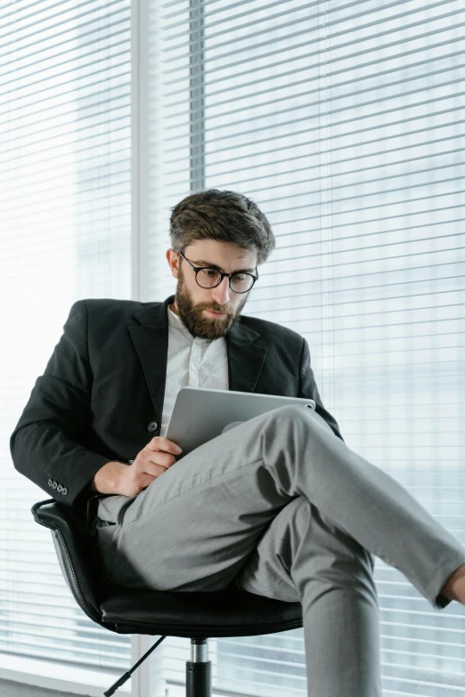 a man sitting in a chair using a tablet computer, trending on pexels, office clothes, man with glasses, grey, awkward