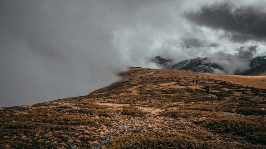 a group of people walking up a hill on a cloudy day, pexels contest winner, alpine climate, thumbnail, brown, spooky photo