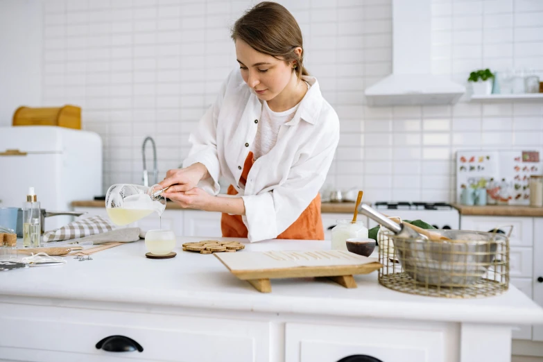 a woman in an apron preparing food in a kitchen, by Julia Pishtar, trending on pexels, lab coat and tee shirt, baking artwork, background image, dessert