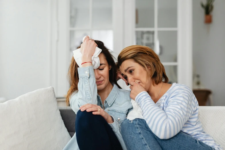 a couple of women sitting on top of a couch, a photo, pexels, hurufiyya, crying one single tear, healthcare, woman holding another woman, spring season