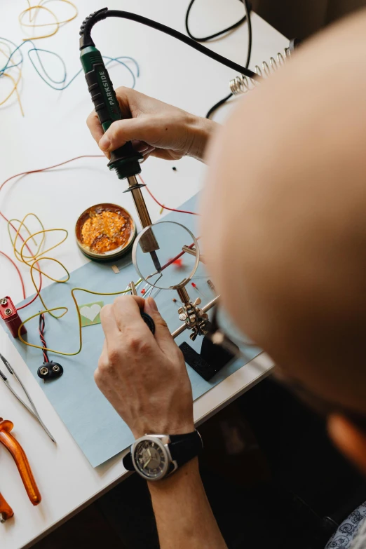 a man sitting at a table working on a project, trending on pexels, revealing wires and electronics, carefully crafted, tools for science research, profile pic