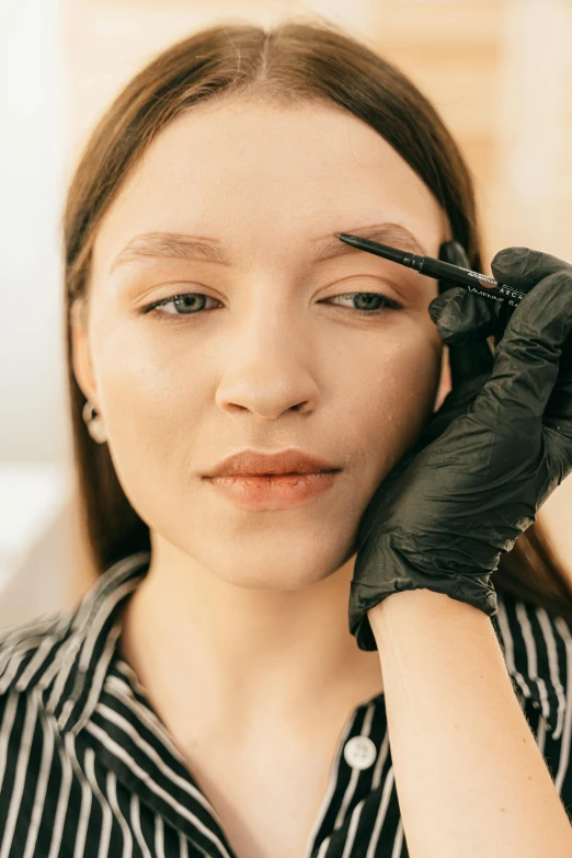 a woman getting her eyebrows done at a beauty salon, a tattoo, by Julia Pishtar, trending on pexels, mannerism, portrait androgynous girl, looking straight, wearing professional makeup, brown