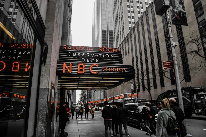 a group of people walking down a street next to tall buildings, by Kristin Nelson, pexels contest winner, art nouveau, television show, marquee, nbc, thumbnail