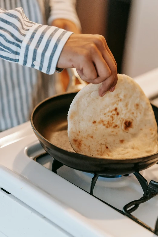 a person putting a tortilla in a pan on a stove, by Julia Pishtar, trending on, south east asian with long, uncrop, panini