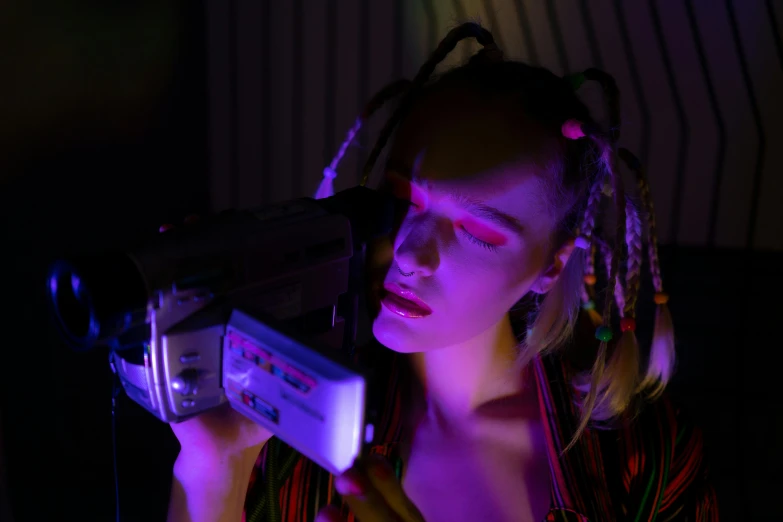 a woman holding a video camera in a dark room, cyberpunk art, trending on pexels, video art, portrait of kim petras, ultraviolet and neon colors, 9 0 s vhs aesthethic, cyberpunk headpiece