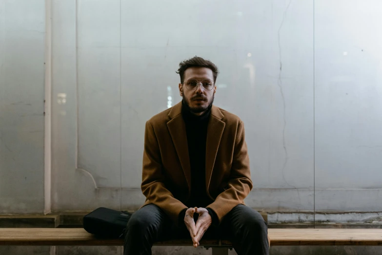 a man sitting on top of a wooden bench, an album cover, by Attila Meszlenyi, pexels contest winner, he is wearing a brown sweater, trench coat and suit, zaha hadi, portrait mode photo