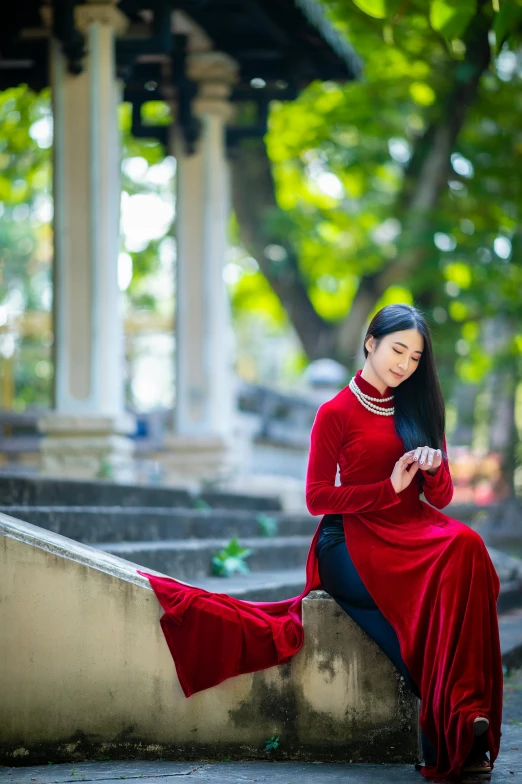 a woman in a red dress sitting on some steps, inspired by Cui Bai, pexels contest winner, ao dai, dressed in velvet, praying, in the park