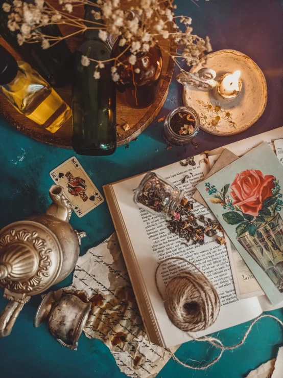 an open book sitting on top of a table next to a candle, a still life, trending on pexels, magical realism, antique perfume, snapchat photo, board games on a table, gold and teal color scheme