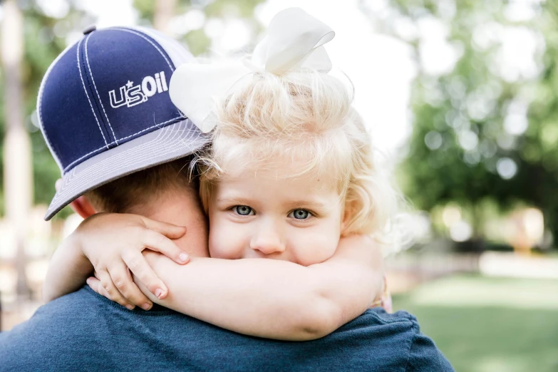 a man holding a little girl in his arms, by Lee Loughridge, unsplash, wearing a navy blue utility cap, sydney hanson, max dennison, uncrop