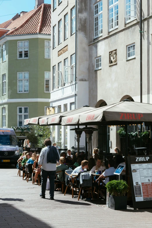 a group of people sitting outside of a restaurant, by Ejnar Nielsen, unsplash, art nouveau, sunny day time, square, denmark, street elevation