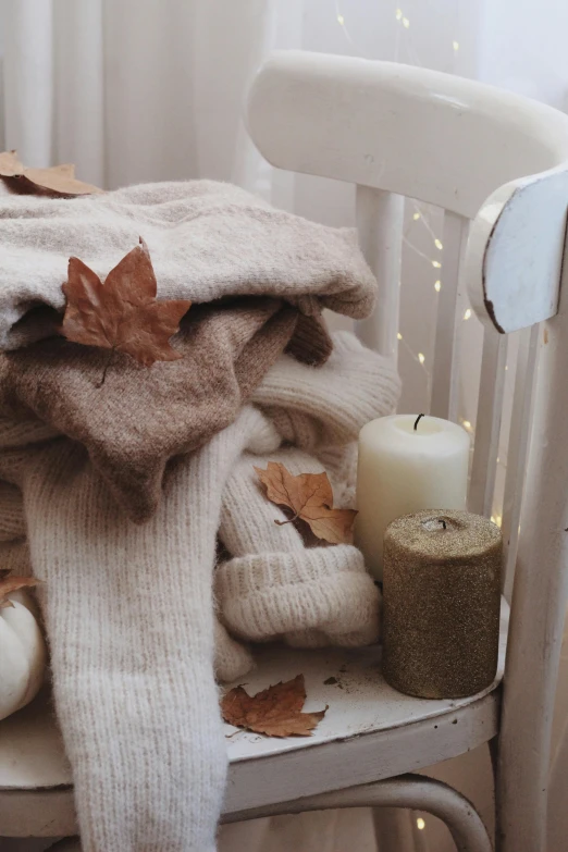 a pile of sweaters sitting on top of a chair, a still life, by Lucia Peka, trending on pexels, natural candle lighting, leafs falling, 🍁 cute, white