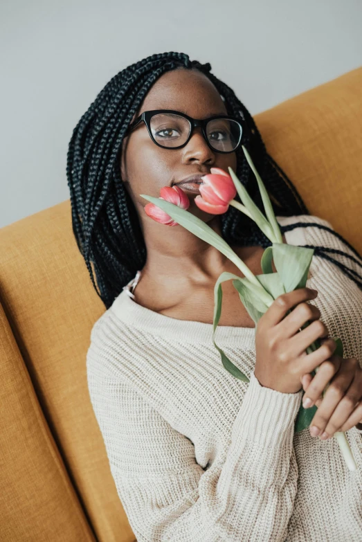 a woman sitting on a couch holding a flower, pexels contest winner, nerdy black girl super hero, tulips, square rimmed glasses, romantic lead