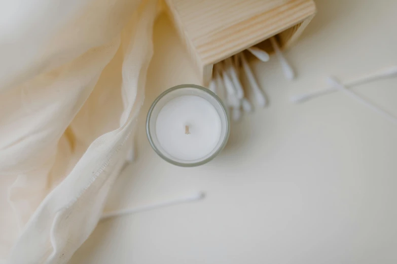 a candle sitting on top of a table next to a brush, unsplash, cream white background, detailed product image, high - angle view, light source from the left