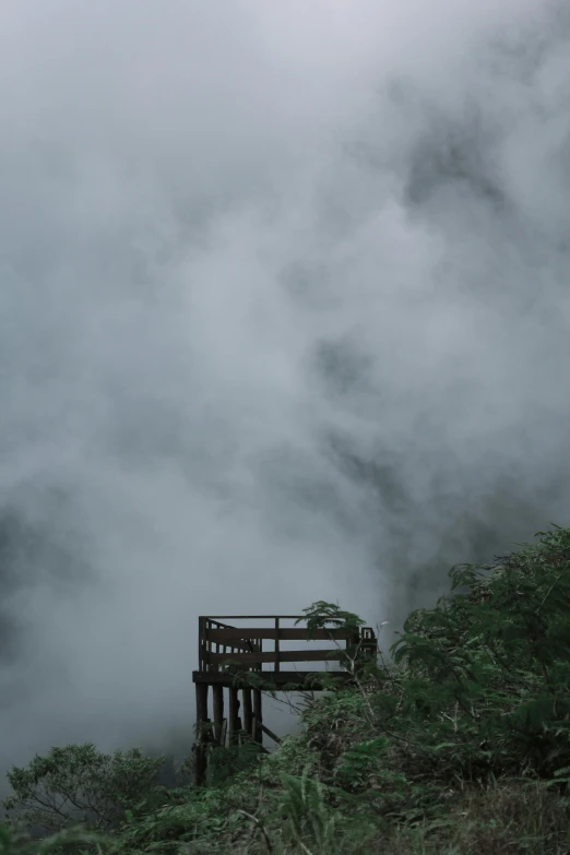 a wooden structure sitting on top of a lush green hillside, pexels contest winner, romanticism, melting volumetric smoke and fog, grey, looking down a cliff, the sky is gray