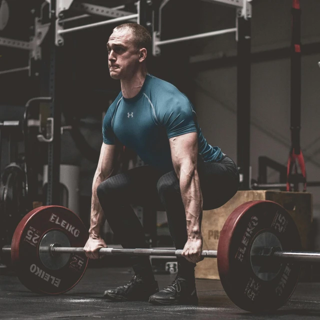 a man squatting with a barbell in a gym, by Emma Andijewska, in a dark teal polo shirt, super high resolution, teal silver red, hybrid human/tank