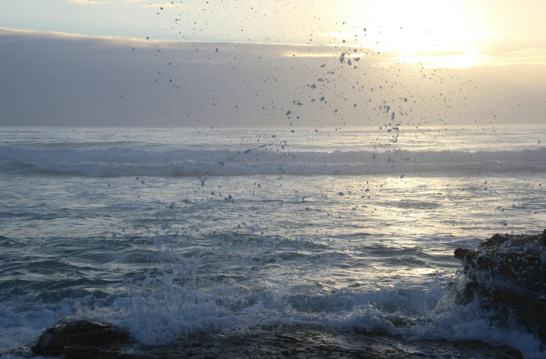 a man standing on top of a rock next to the ocean, hurufiyya, splashing water, early evening, lots of bubbles, soaring waves