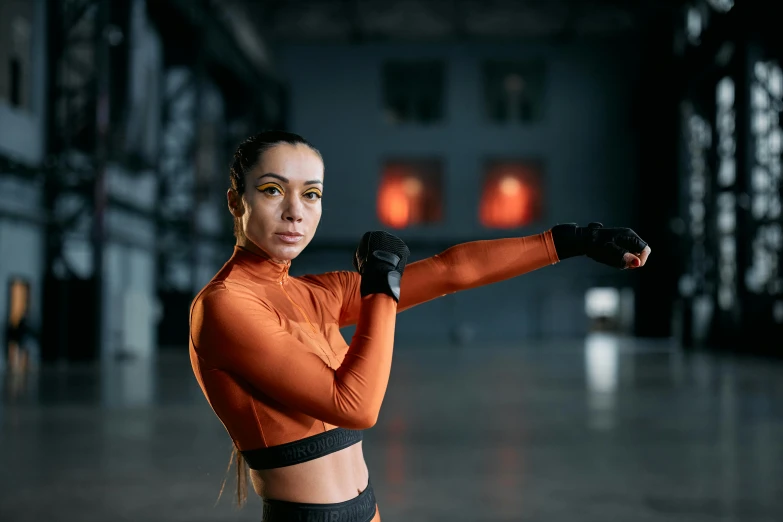 a woman in an orange top holding a baseball bat, by Emma Andijewska, pexels contest winner, mma southpaw stance, dua lipa, elbow gloves, wearing a tracksuit